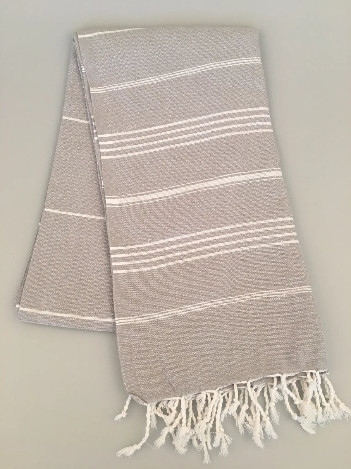 Light gray Turkish towel with white stripes and fringed edges, folded on a neutral background.