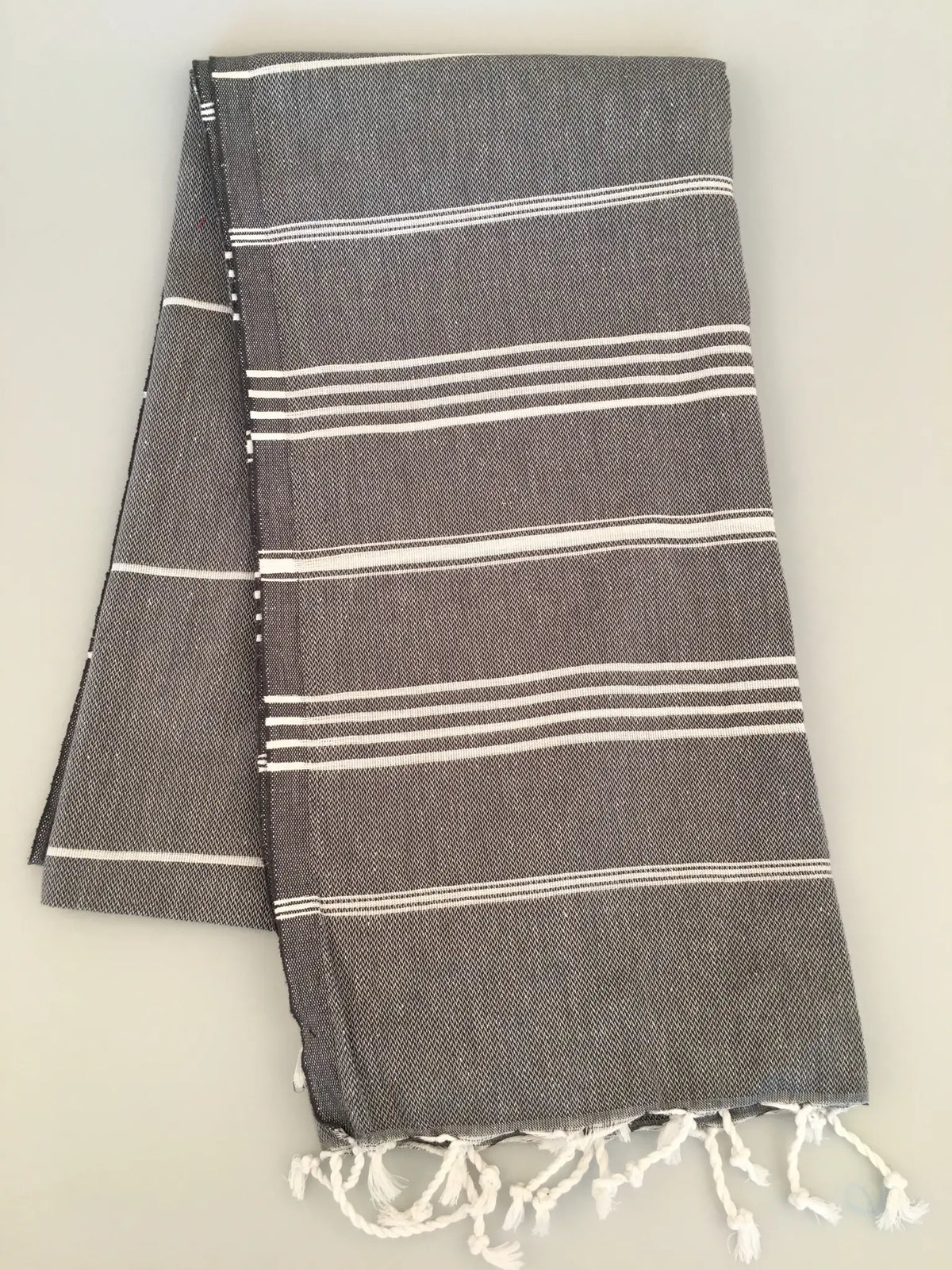 Gray Turkish towel with white stripes and fringed edges, folded neatly, showing soft texture and a lightweight design.